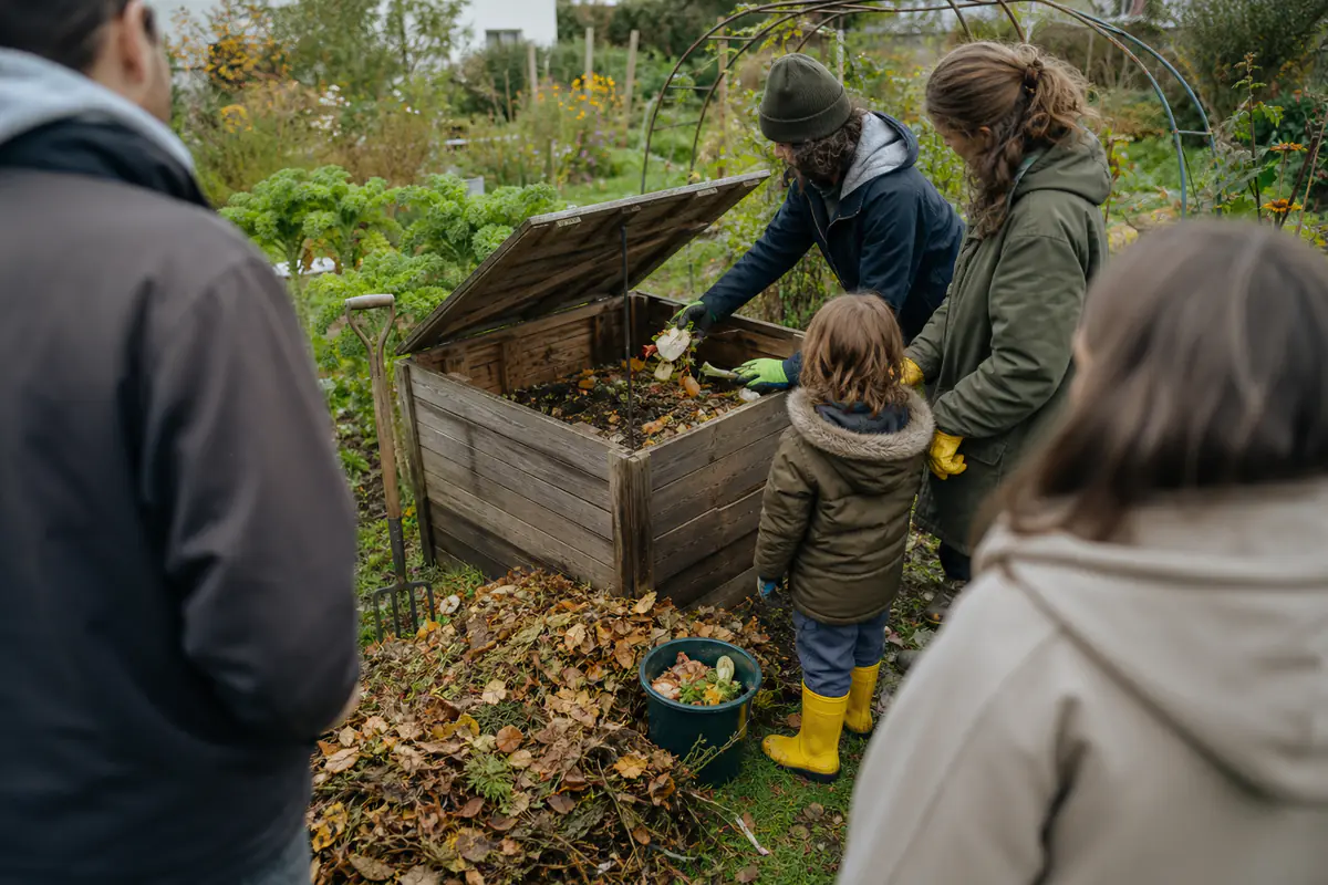 Jardiniers autour d’un composteur et d’un arceau métallique dans un potager familial français lumineux
