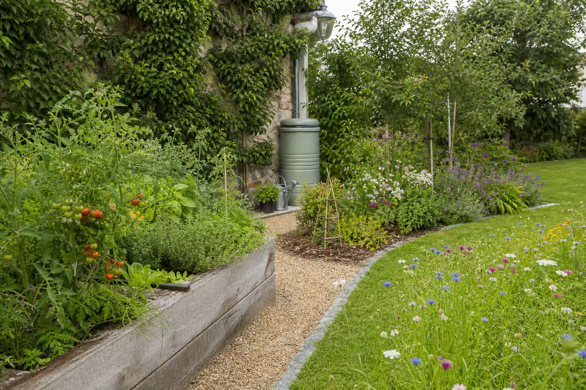 Jardin familial français avec paillage, massif fleuri, potager en bacs et zone de pelouse volontairement haute.