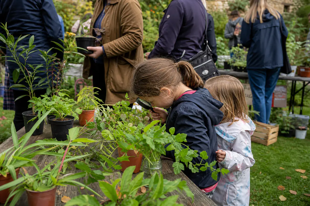 Tables de plantes étiquetées et familles participant à des animations lors d’un vide-jardins convivial
